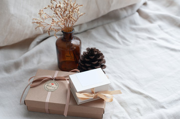 A white picture frame placed in a brown gift box surrounded by a box of small diamond rings tied with cream-colored pine cones dried flowers in a brown glass bottle. Put on a light brown fabric