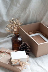 A white picture frame placed in a brown gift box surrounded by a box of small diamond rings tied with cream-colored pine cones dried flowers in a brown glass bottle. Put on a light brown fabric
