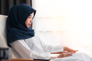 A young Asian Muslim woman wearing a dark blue hijab and cross-over headscarf. Sitting and thinking...