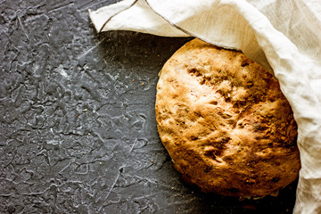 A loaf of round homemade bread with nuts on a dark background, next to a cotton napkin. Top view, copy space