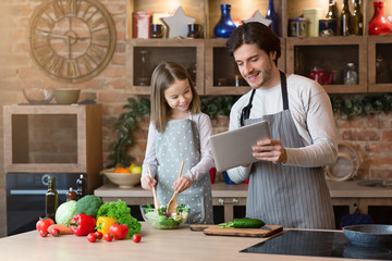 Dad and little daughter reading recipe on digital tablet, cooking together