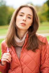 Close up portrait of a young beautiful brunette girl in coral coat