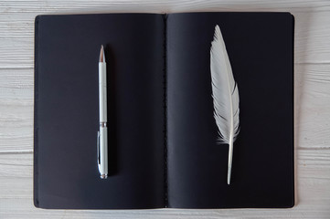 Old and new concept for history novel book, writer work, white feather and pen on black paper notebook,  black and white, minimalism