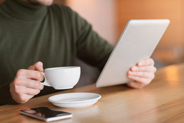 Male hands holding cup of tea and digital tablet