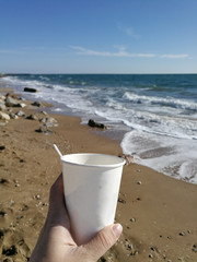 Fototapeta na wymiar Man's hand holding a cup of coffee against the ocean.