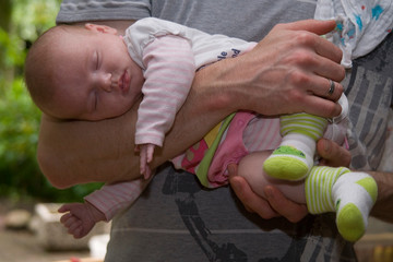 Baby liegt im Fliegergriff auf dem Unterarm und schläft