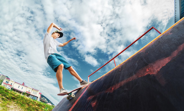 Portrait Of A Young Skateboarder Doing A Trick On His Skateboard On A Halfpipe Ramp In A Skate Park In The Summer On A Sunny Day. The Concept Of Youth Culture Of Leisure And Sports