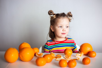 Fototapeta na wymiar Little girl, 3 year old baby, with a ponytail hairstyle in a colorful colorful striped jacket with a huge number of appelsins and tangerines