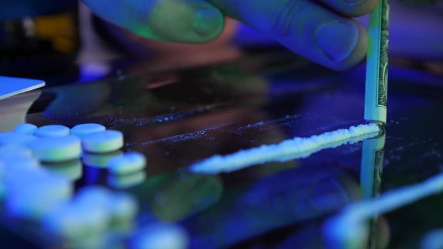 Drug addict concept: hard drugs prepared for consumption. Cocaine, amphetamine, meth, methamphetamine. Silver tray with powder drugs, money and pills. Man draw in or sniff white drug.