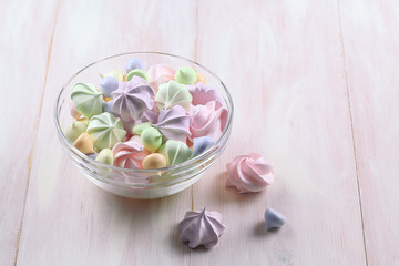 Colored Meringue Cookies in a transparent glass bowl, on a light wooden background.