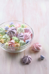 Colored Meringue Cookies in a transparent glass bowl, on a light wooden background.