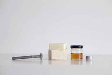 Zero waste bathroom products on a table. Safety razor, soap bar, oil in a glass bottle and small aluminium can.