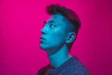 Portrait of a guy with colorful neon light on pink studio background. Male model with calm and...