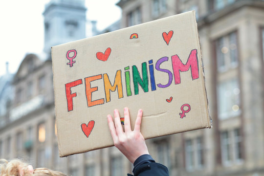 Woman's hand holding a rainbow colored sign saying Feminism