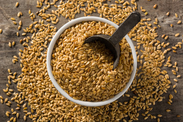 Golden flax seeds in white bow on wooden table. Top view	