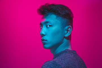 Portrait of a guy with colorful neon light on pink studio background. Male model with calm and...