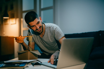 young man working late from his home, eating chinese food