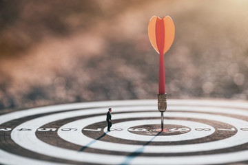Businessman standing lookup red dart arrow hitting target centre dartboard on sunset background....