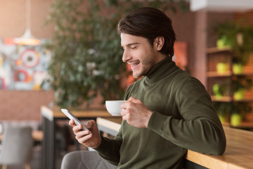 Prosperous businessman having coffee break at cafe, using smartphone