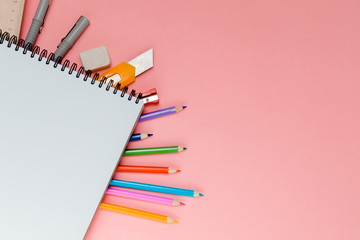 Colorful school supplies under  spiral notepad on pink background with place for text. Stationery...