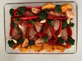 Juicy chicken thighs covered with vegetables broccoli potatoes and garlic in a plate for baking.