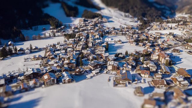 A tilt-shift video. Aerial view of the small town of Al Plan in the Italian Dolomites. Hundreds of small houses, snow covering streets and fields, smoke is rising from the chimneys.