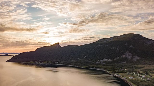 A magnificent sunset on Senja Island. The sun cast its rays down upon the clouds painting them in warm hues of yellow, gold and orange.  Reflection playing on the mirrorlike sea surface.