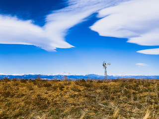 Fototapeta na wymiar A old fashioned windmill sits atop a grassy hill with blue sky and beautiful clouds.
