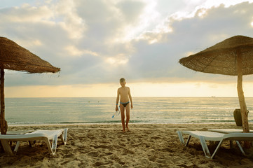A boy on the background of the sea and cloudy sky walks along the beach after swimming with a mask for snorkeling © Viktoryia