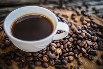  Black coffee in a white cup With freshly roasted coffee beans spilled on a wooden table