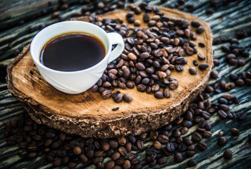  Black coffee in a white cup With freshly roasted coffee beans spilled on a wooden table
