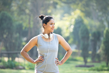 Fit woman in sportswear listening music on headphones at park outdoor