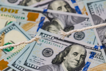Closeup of frayed breaking rope with 100 dollar bills in background. Concept of fragile economy, stock market crash, and recession