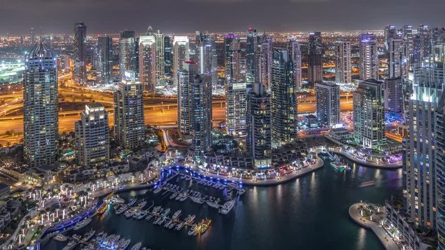 Dubai Marina illuminated skyscrapers and jumeirah lake towers panoramic view from the top aerial night timelapse in the United Arab Emirates. Traffic on a road and floating yachts