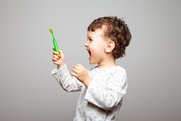 boy looks at a new toothbrush. strong joy, wild delight, a look to the side. hygiene rules. child stands on a gray background, studio, isolated