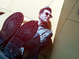A handsome young pilot sitting on the wing of a plane