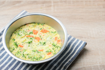 Top view of Homemade steamed egg with​ carrot, broccoli, onion and​ ​ mixed vegetables​ on​ wooden​ background.​ Asian Healthy​ food​ for​ kid​ age 1-3​ years​ old or for all family members.