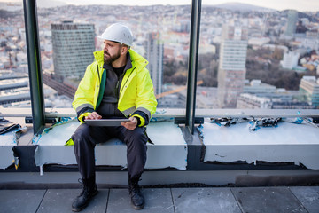 Man engineer sitting on construction site, holding tablet.