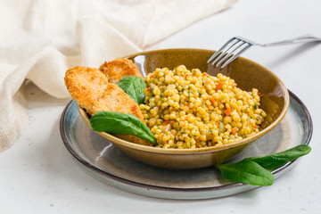 Homemade Ptitim with chicken schnitzel. Ptitim - or Israeli couscous - toasted paste. Made with fried onion, carrot, tomato and spinach.