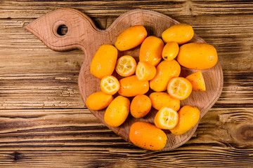 Cutting board with kumquat fruits on wooden table. Top view