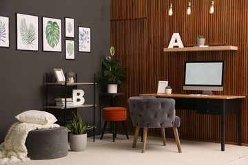 Comfortable workplace with computer near wooden wall in stylish room interior. Home office design