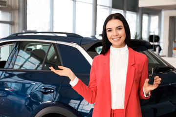 Fototapeta na wymiar Saleswoman with key near car in dealership