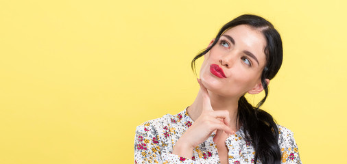 Young woman in a thoughtful pose on a yellow background