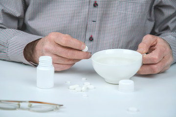 senior man holding pill and cup with water at white table