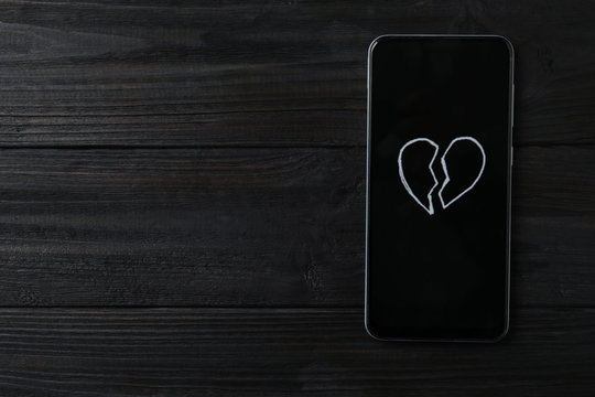 Smartphone with picture of broken heart and space for text on black wooden background, top view. Relationship problems concept
