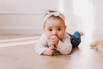 Naklejka premium Baby girl portrait with teether in mouth on the floor.