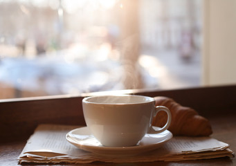 Delicious morning coffee, newspaper and croissant near window, indoors