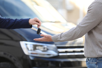 Obraz na płótnie Canvas Salesman giving key to customer in modern auto dealership, closeup. Buying new car