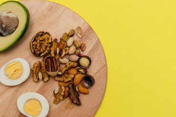 Flat lay ketogenic diet. Аvocado,egg and nuts on the wooden cutting board on the yellow background. Concept of healthy food.Copy space for mock up