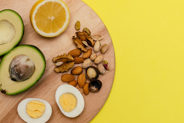 Flat lay ketogenic diet. Аvocado,eggs,lemon,nuts on the wooden cutting board on the yellow background. Concept of healthy food.Copy space for mock up